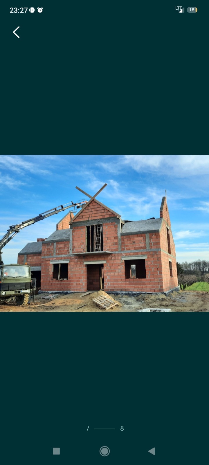 Wznoszenie dwukondygnacyjnego domu z czerwonej cegły w Gozdowie, widoczny dźwig budowlany i częściowo położony dach.