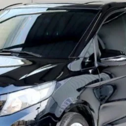 Błyszczący, czarny Mercedes-Benz Vito z przyciemnianymi szybami, zaparkowany w jasnym pomieszczeniu, widok z przodu i boku.