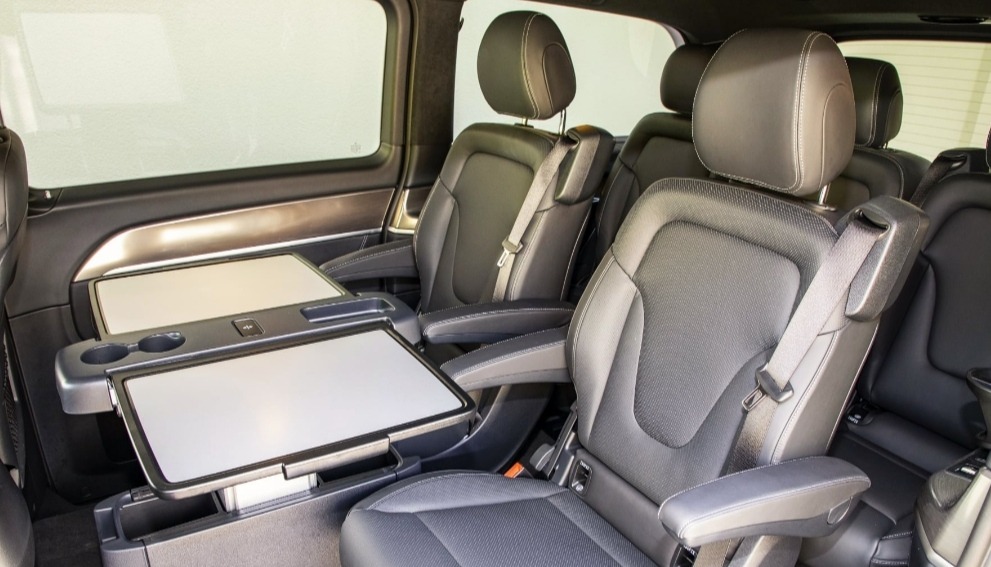 Wnętrze luksusowego busa z czarnymi skórzanymi fotelami, rozkładanymi stolikami i uchwytami na napoje.