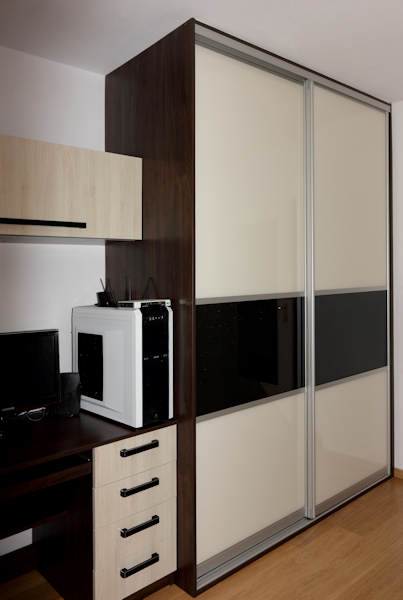 Szafa wnękowa z przesuwnymi drzwiami w kolorze beżowym i czarnym, wkomponowana w zabudowę z biurkiem i szafkami w odcieniach brązu i beżu, obok stoi komputer stacjonarny.