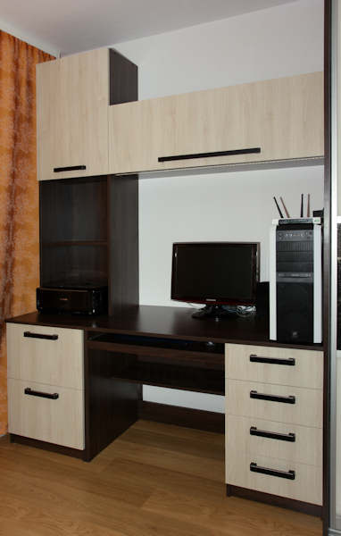 Zestaw mebli biurowych z biurkiem, szafkami wiszącymi i szufladami w odcieniach brązu i beżu, z czarnymi uchwytami, uzupełniony komputerem stacjonarnym i monitorem.