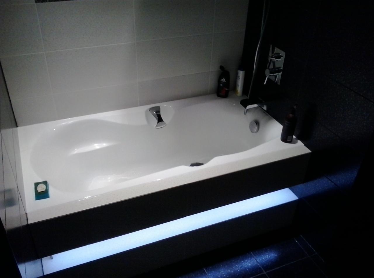 Biała wanna z chromowaną armaturą w nowoczesnej łazience z podświetleniem LED na obudowie wanny.