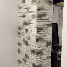 Wykończenie ściany imitujące kamień w odcieniach szarości i bieli, tworzące dekoracyjny element architektoniczny przy wejściu do kuchni z widoczną kuchenką gazową.