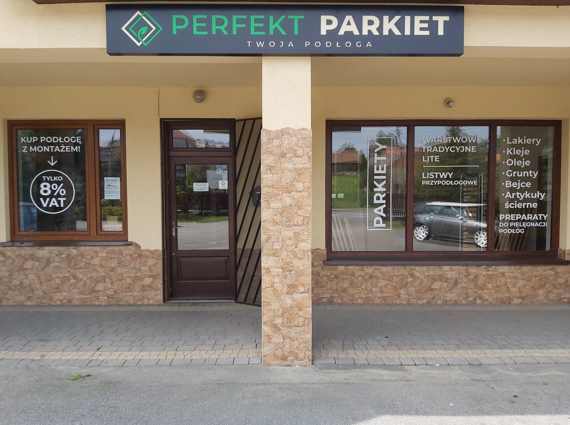 Fasada sklepu z parkietami 'Perfekt Parkiet', widoczne okna z ekspozycją produktów, szyld z nazwą i logo firmy, oraz informacja o 8% VAT na podłogi z montażem.