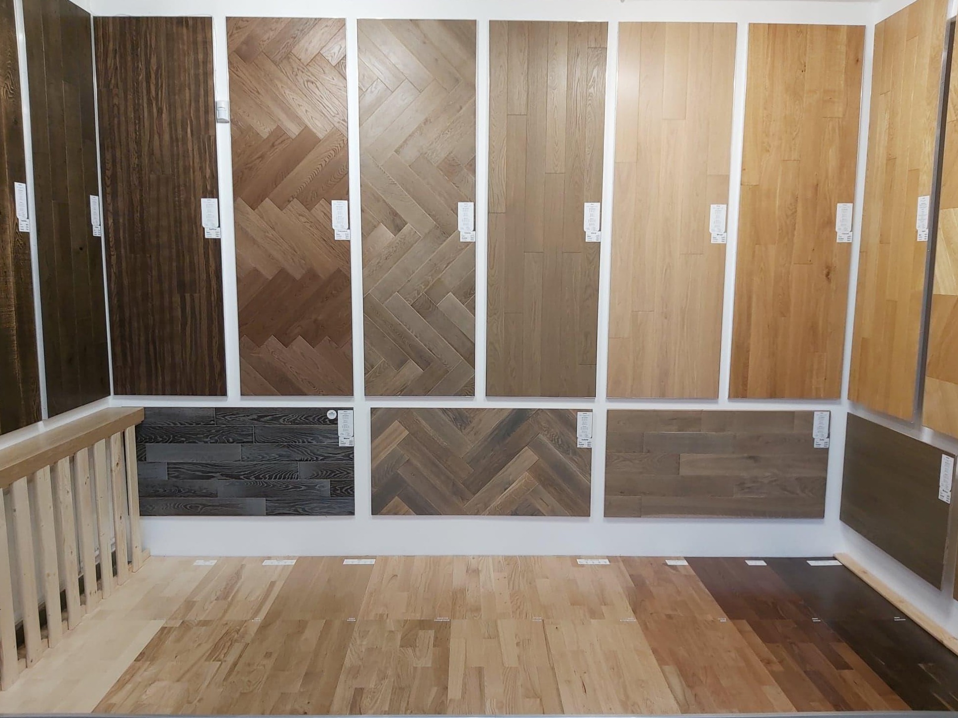 Ekspozycja różnych wzorów i kolorów paneli i desek podłogowych, w tym wzór jodełki, prezentowana w salonie sprzedaży.