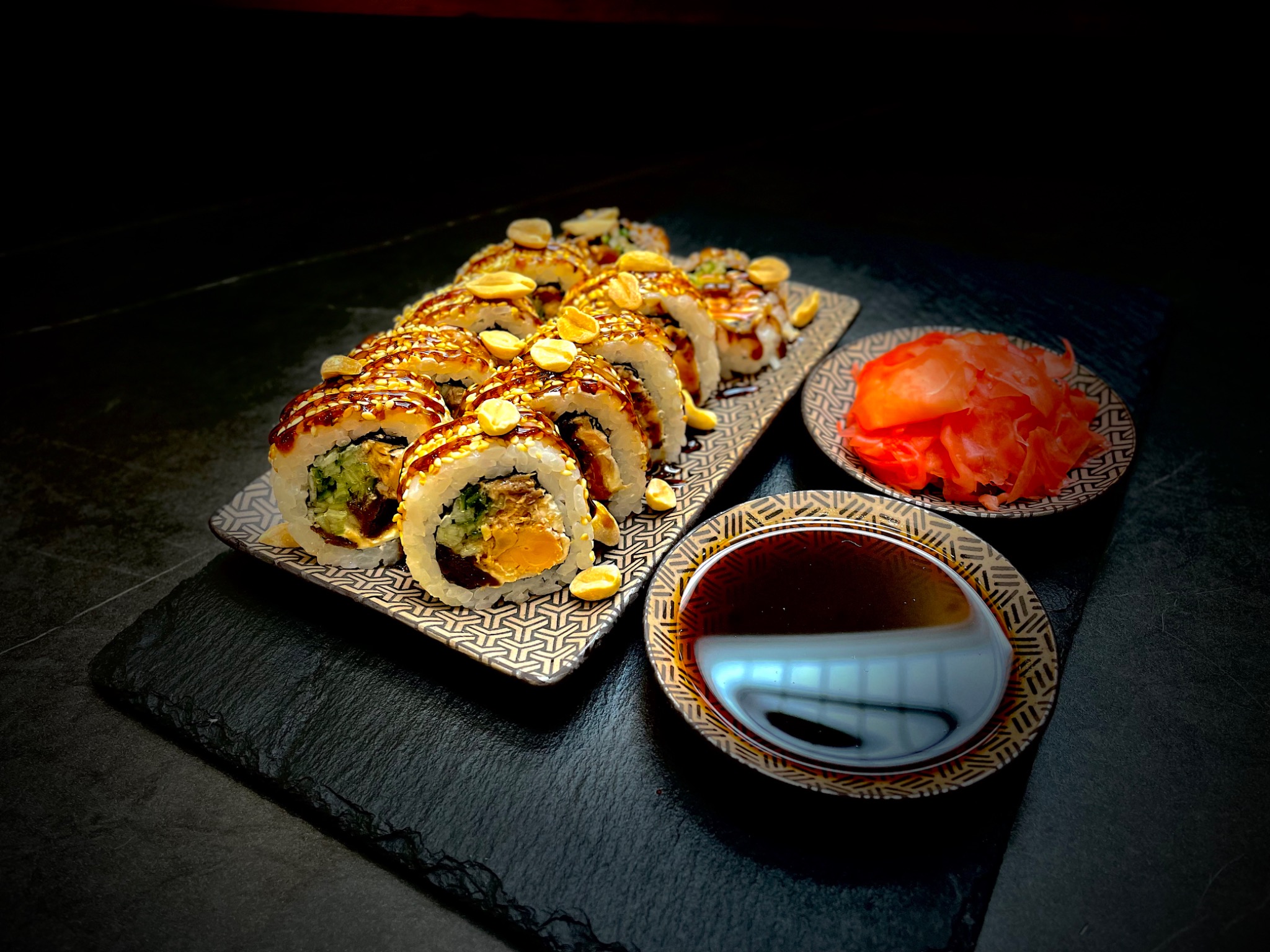 Elegancko podane sushi z orzechami i sosem na geometrycznym talerzu, obok imbir i sos sojowy, na czarnym kamiennym tle.