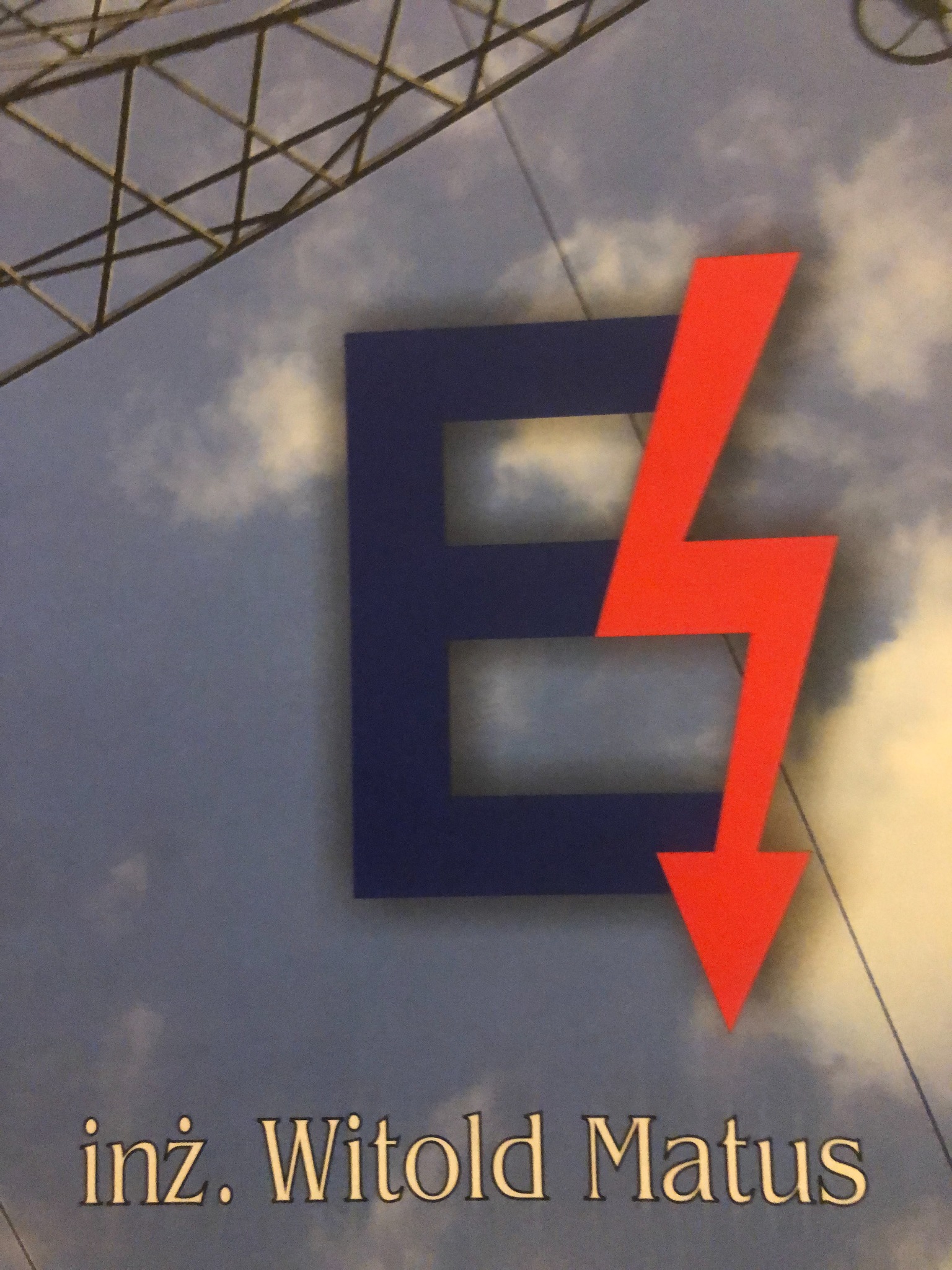 Logo firmy z niebieską literą E i czerwoną strzałką w kształcie błyskawicy na tle nieba i fragmentu konstrukcji stalowej, podpisane 'inż. Witold Matus'.