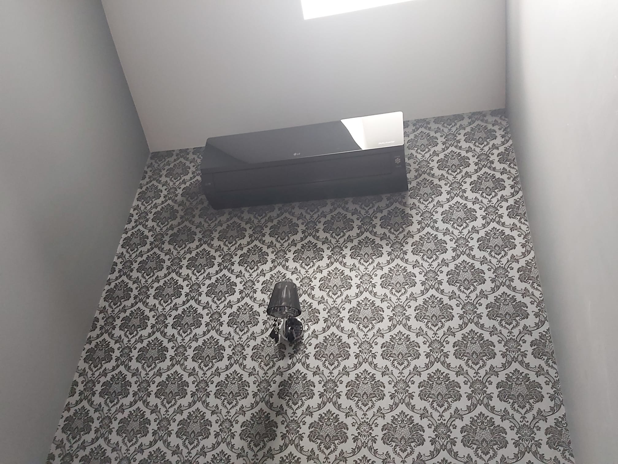 Czarny klimatyzator LG zamontowany na ścianie z wzorzystą tapetą w pomieszczeniu z oświetleniem sufitowym i kinkietem.
