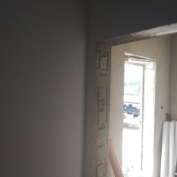 Rafcio - Surowy ościeża drzwi po szpachlowaniu, widoczne niedoskonałości i faktura, ściana w szarym odcieniu, przygotowania do dalszych prac wykończeniowych.