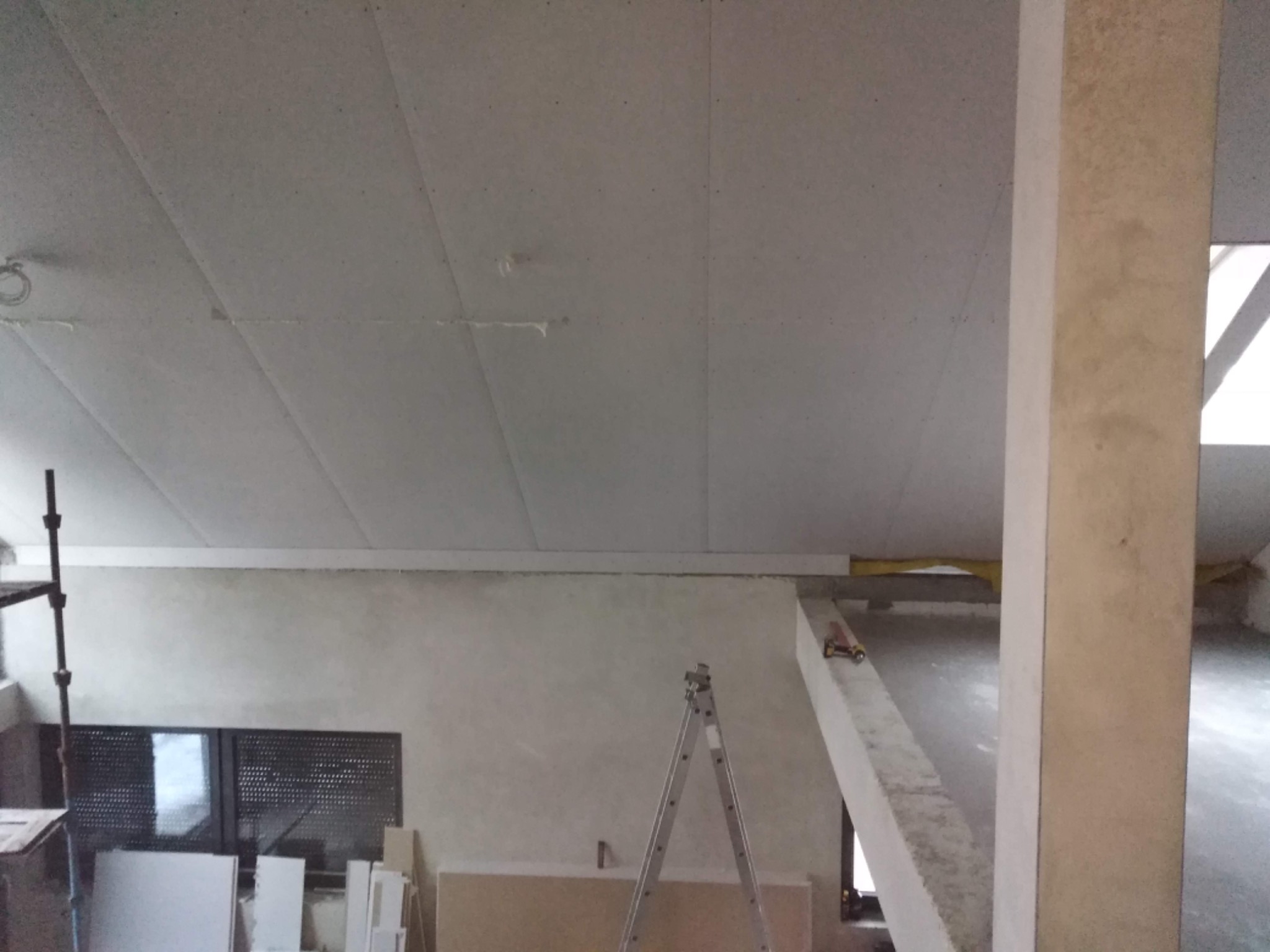 Wnętrze w trakcie prac wykończeniowych: sufit z płyt kartonowo-gipsowych, szpachlowane ściany, aluminiowa drabina rozstawiona w pomieszczeniu.