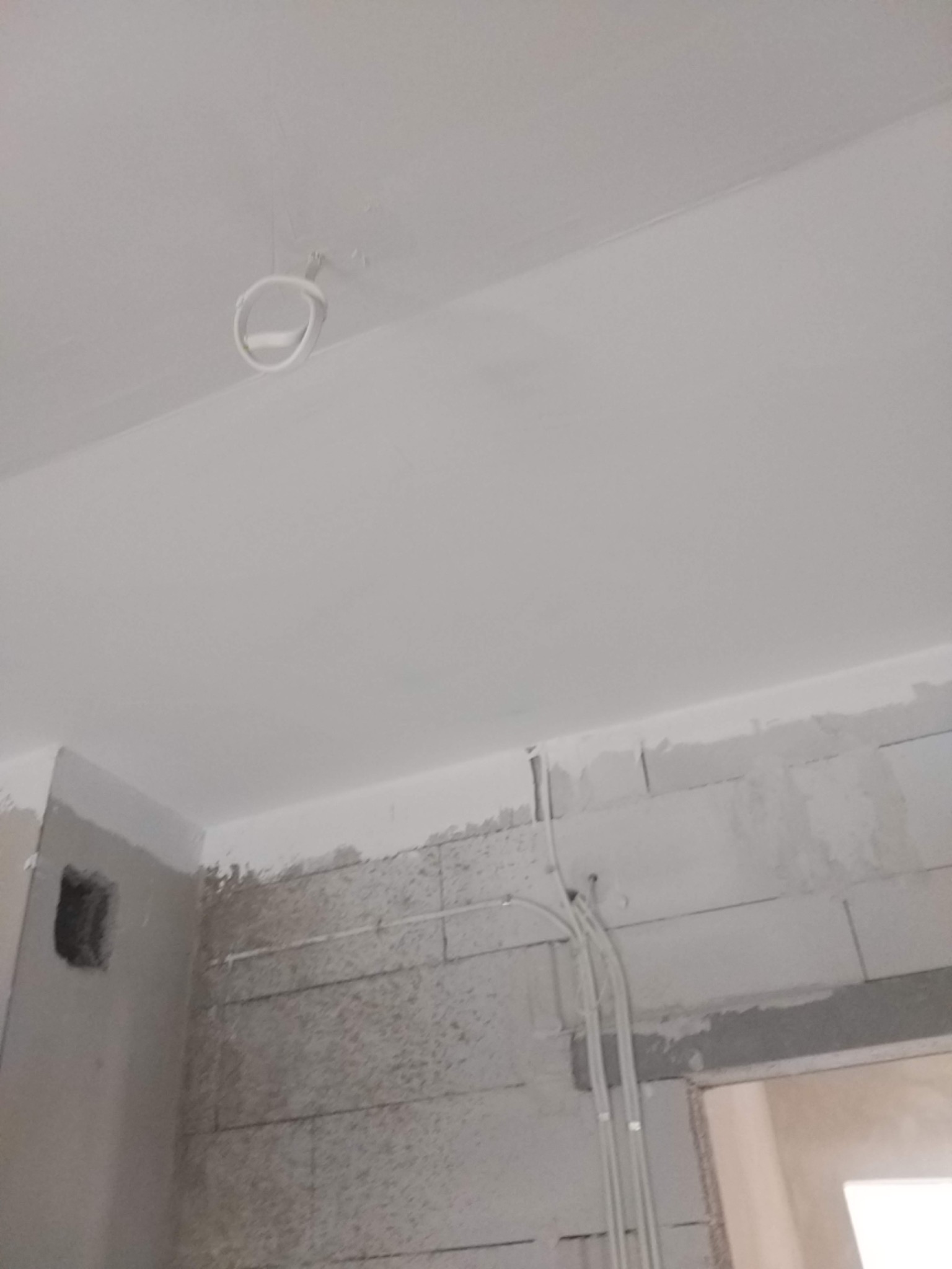 Wnętrze w trakcie remontu: surowy mur z widocznymi przewodami elektrycznymi, świeżo pomalowany sufit z wystającym kablem oświetleniowym.