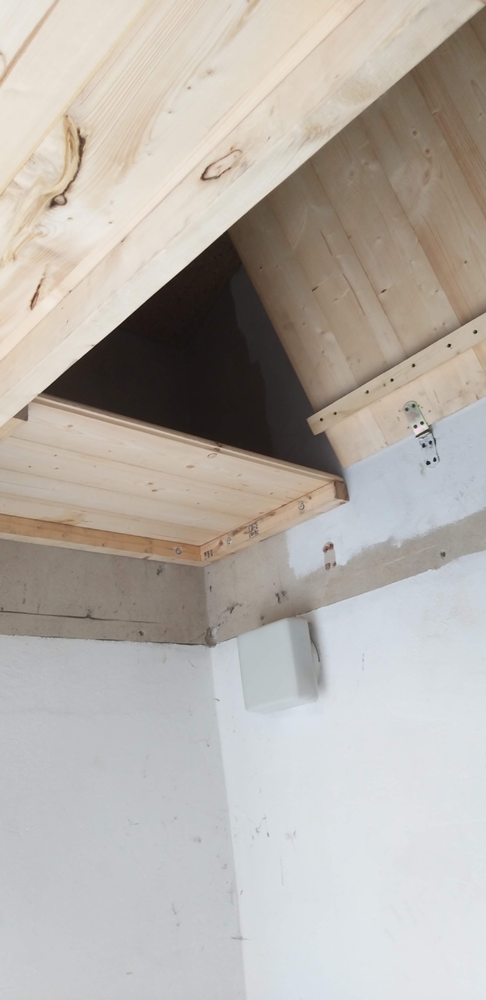 Otwarty drewniany właz strychowy z widoczną konstrukcją mocowania, surowa ściana w tle przed malowaniem.