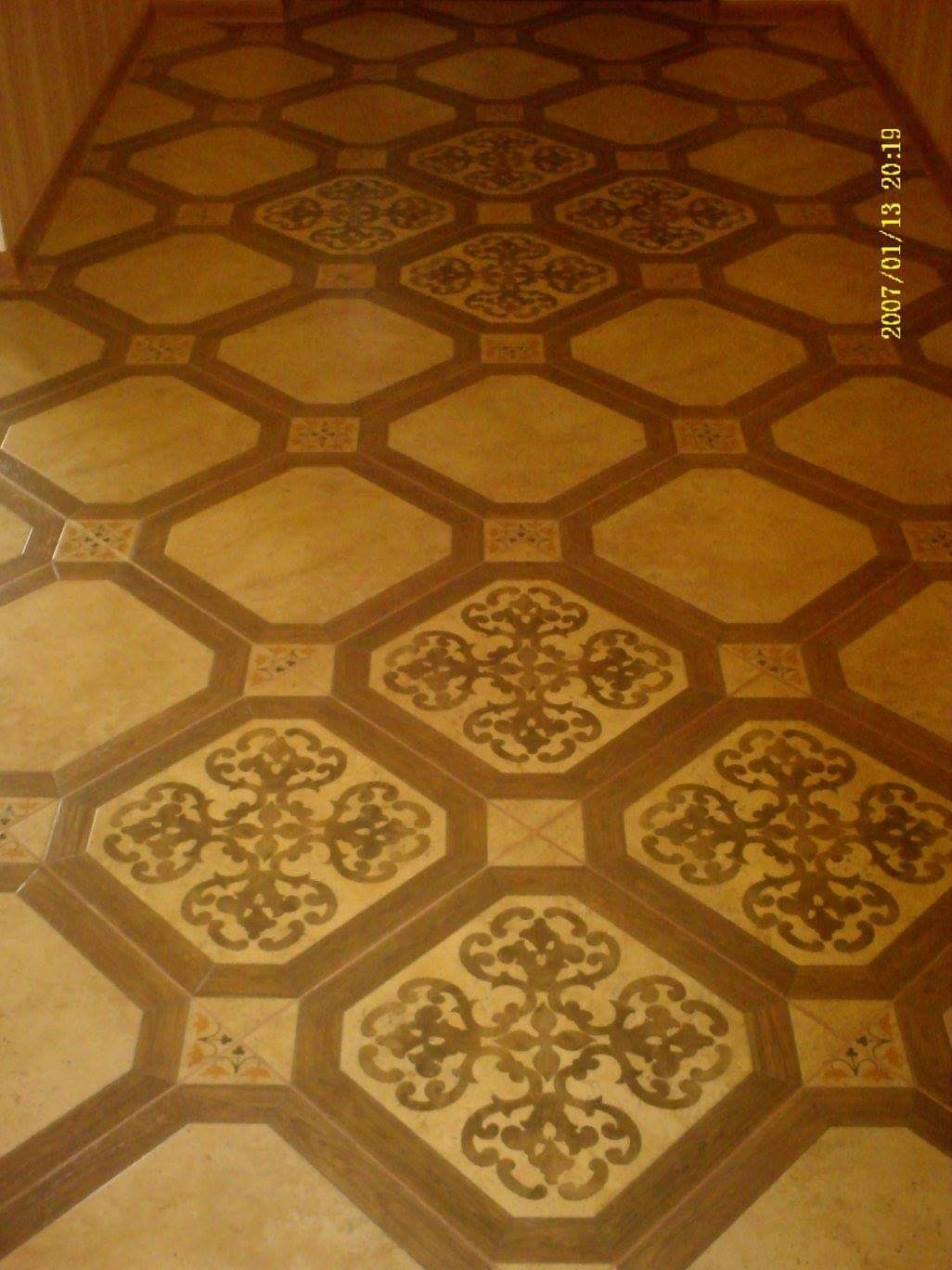 Ułożona podłoga z płytek w geometryczne wzory z motywami roślinnymi, w odcieniach beżu i brązu, sfotografowana z góry pod kątem.