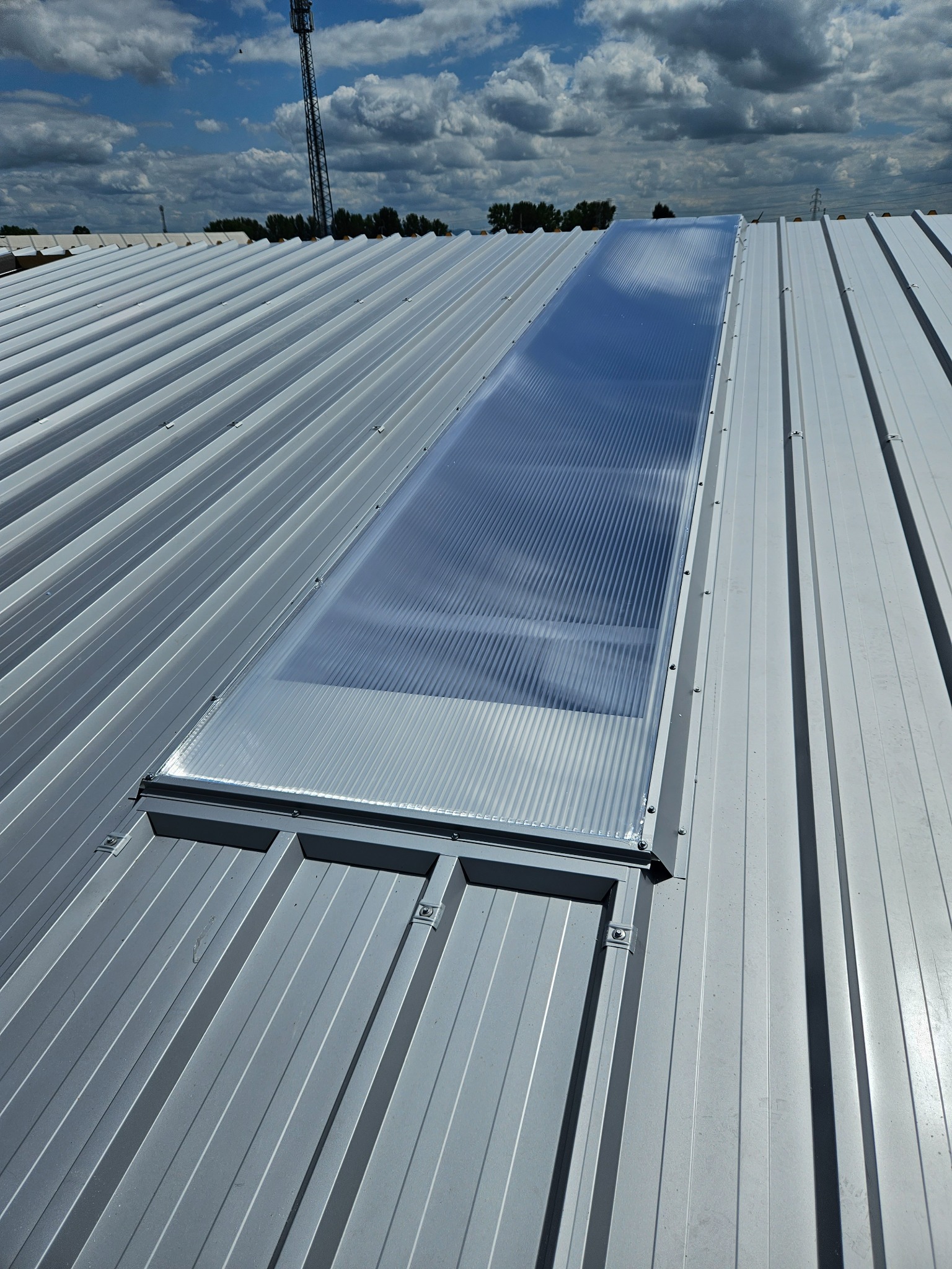 Szary dach z blachy trapezowej z wbudowanym świetlikiem z poliwęglanu, widok z góry w słoneczny dzień.