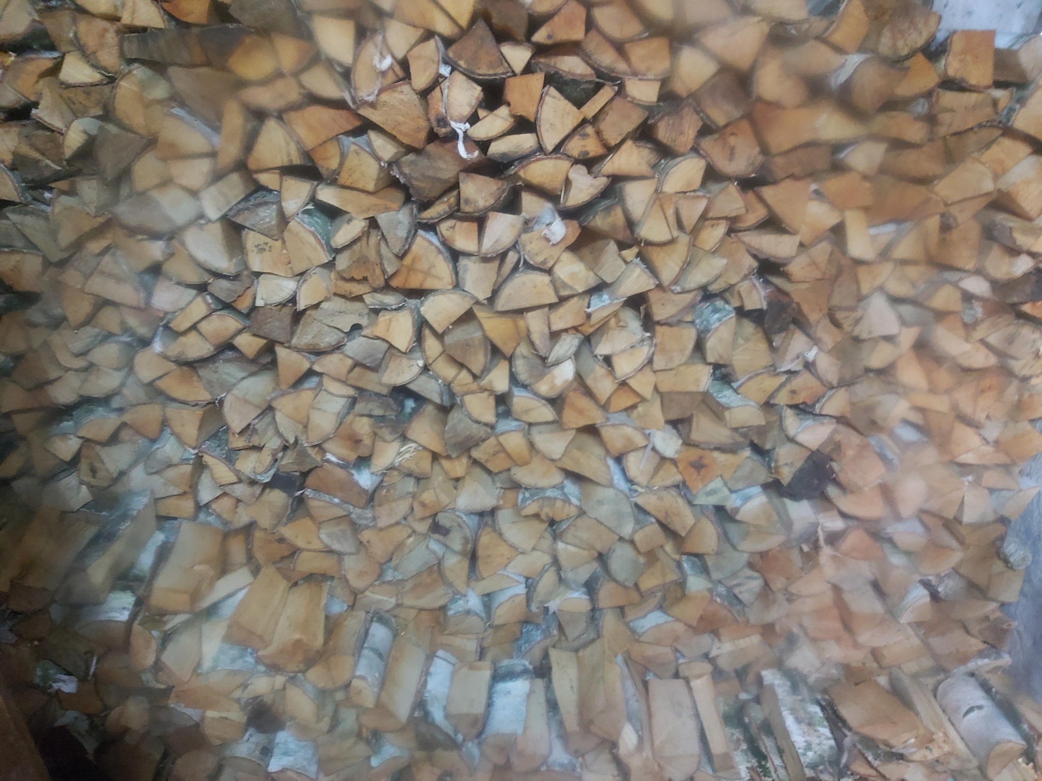 Ułożone, pocięte kawałki drewna z widoczną korą, tworzące teksturę, lekko zamglone ujęcie.