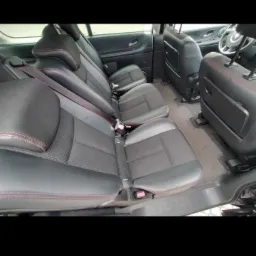 Wnętrze przestronnego samochodu typu van z trzema rzędami czarnych skórzanych foteli z czerwonymi przeszyciami, widok z tyłu kabiny.