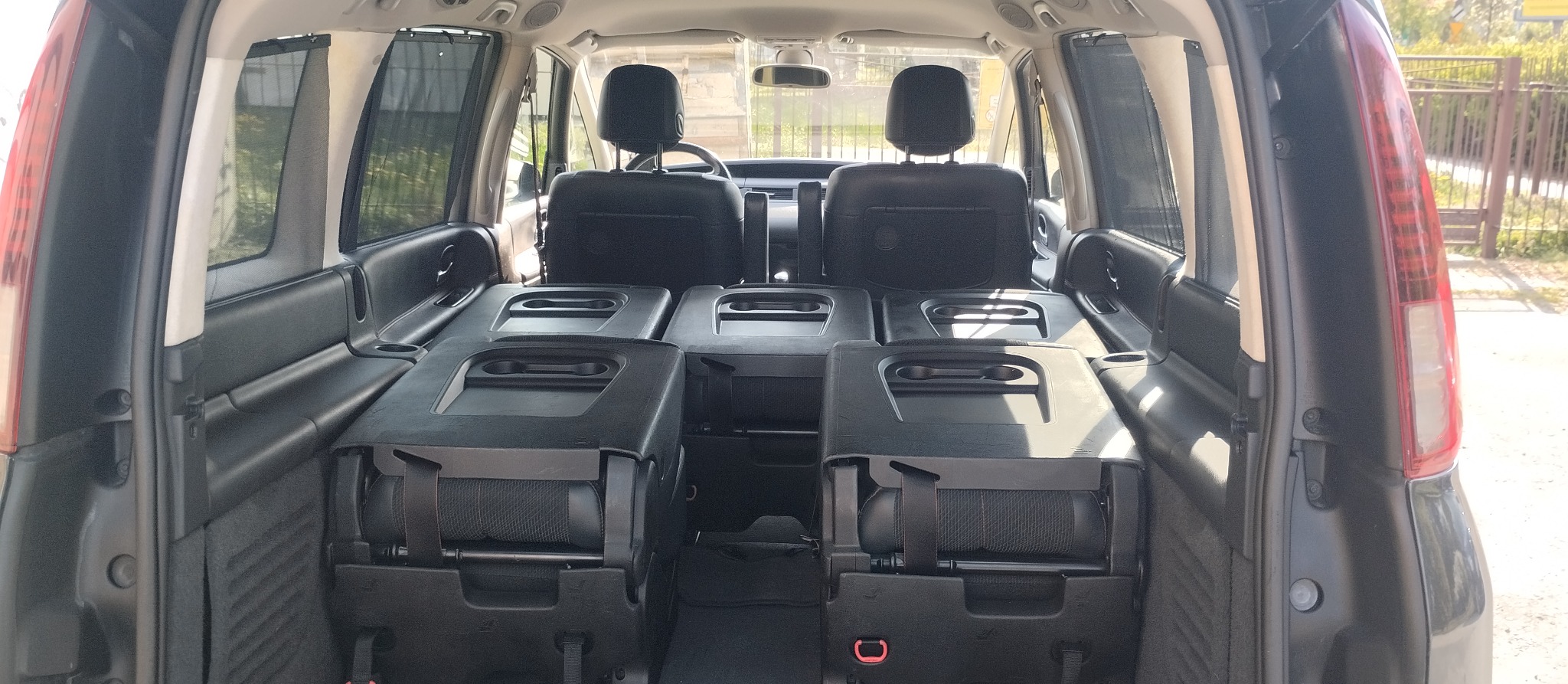 Wnętrze samochodu z rozłożonymi siedzeniami, widok od tyłu, ciemna tapicerka, rolety przeciwsłoneczne w oknach.