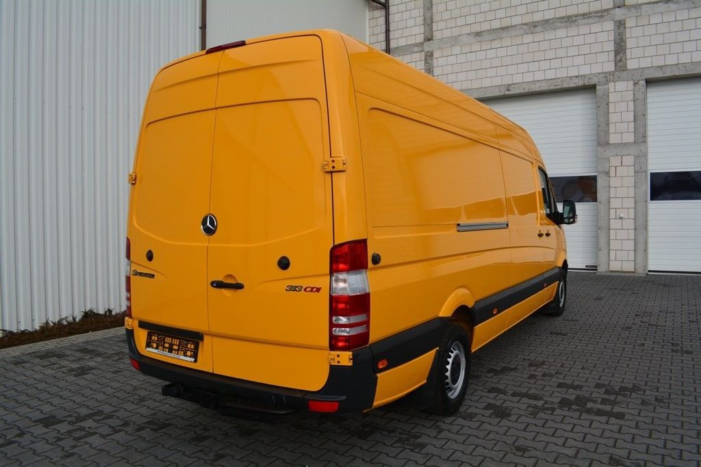 Żółty samochód dostawczy Mercedes Sprinter 313 CDI zaparkowany na kostce brukowej przed budynkiem z bramami garażowymi.