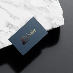 Granatowa wizytówka z tłoczonym złotym logo Babelle na marmurowym tle.