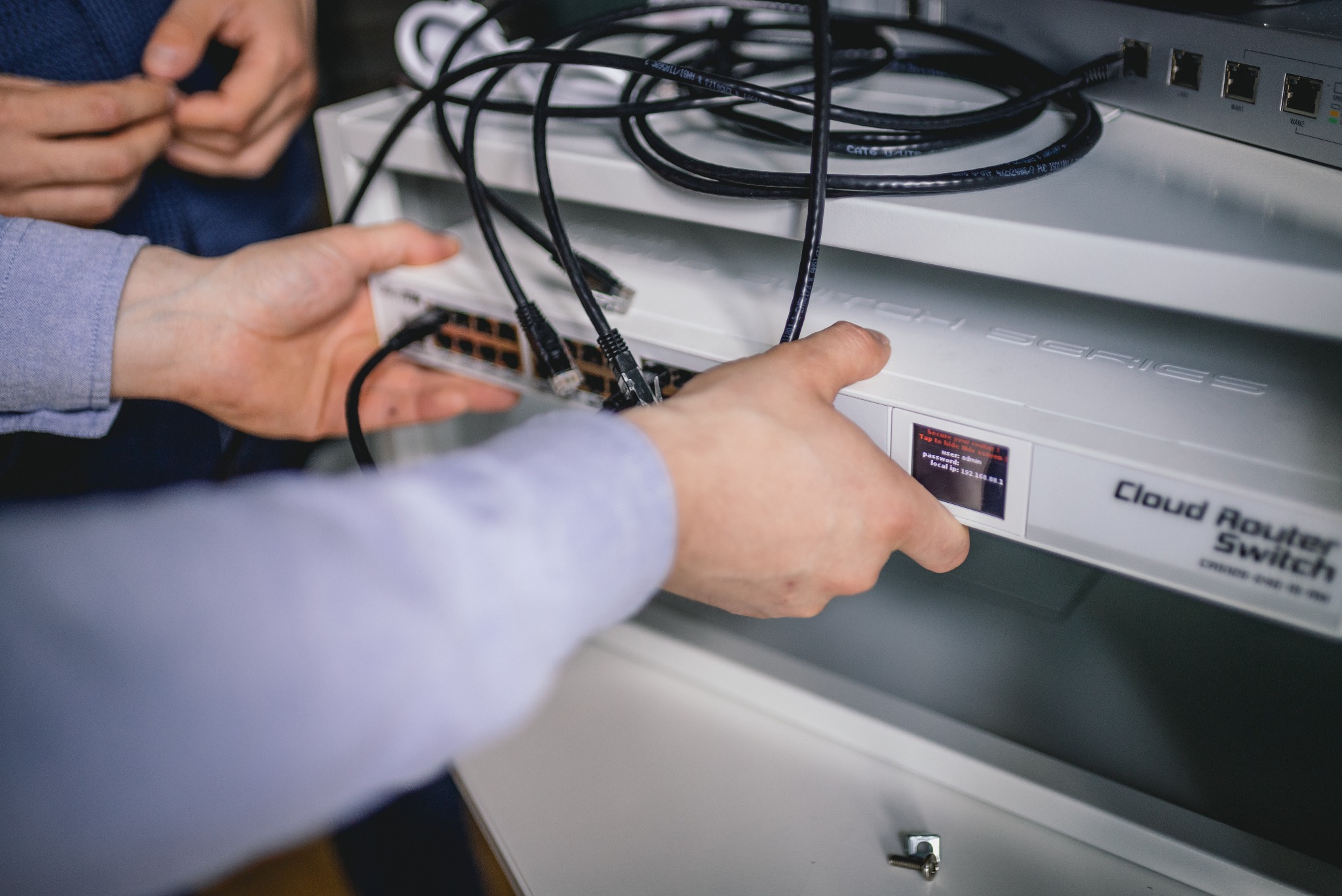 Instalacja Cloud Router Switch w szafie rack, widoczne ręce podłączające kable Ethernet, konfiguracja urządzenia.