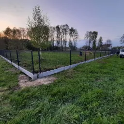 Nowo postawione ogrodzenie panelowe z podmurówką z bloczków betonowych, widok na posesję i okolicę w tle o zmierzchu.