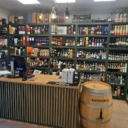 Regały z alkoholem za drewnianą ladą w sklepie w Łodzi, z beczką z napisem Barahonda po prawej stronie.