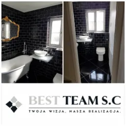 Wykończona łazienka z czarnymi płytkami, białą wanną na nóżkach, umywalką nablatową na białej półce i złotym lustrem w ozdobnej ramie. Widoczny również fragment toalety i grzejnika. Na dole logo...