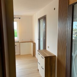 BUILDMEB Paweł Włodarczyk - Nowoczesny przedpokój z drewnianą zabudową, białą komodą z drewnianym blatem, lamelami na ścianie i przeszklonymi drzwiami, widok z korytarza.