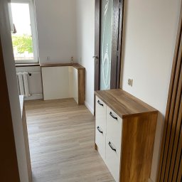 BUILDMEB Paweł Włodarczyk - Nowoczesna szafka z białymi frontami i drewnianym blatem w przedpokoju, obok drzwi z matowym szkłem i dekoracyjnej ściany z drewnianych listew.