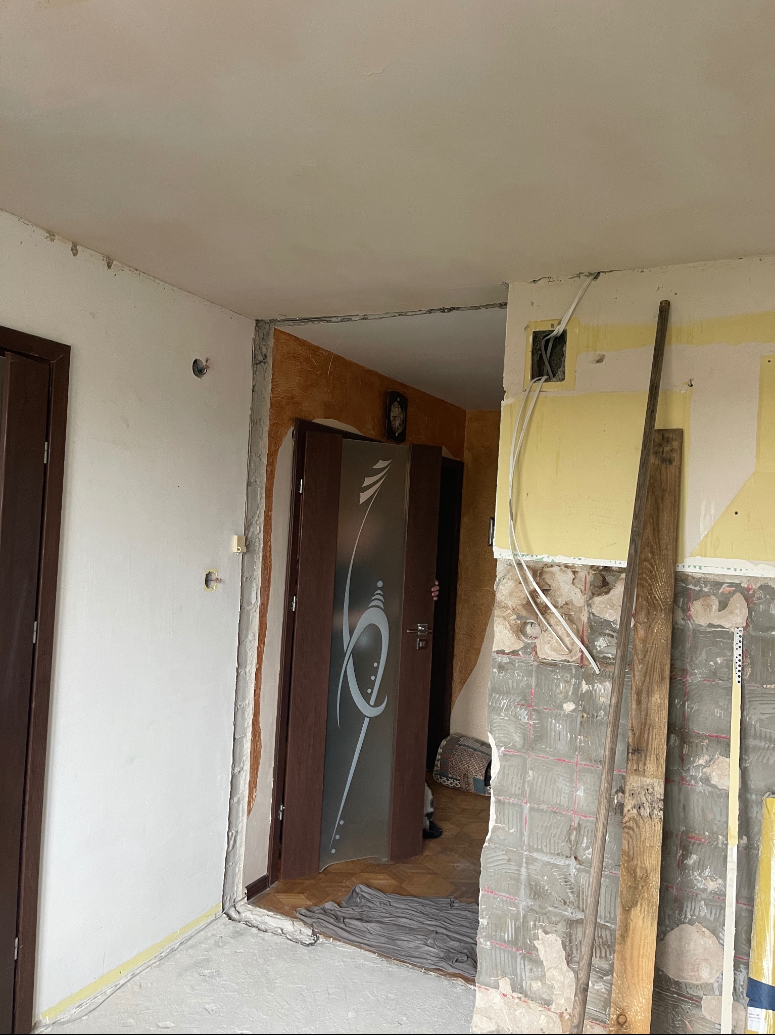 Wnętrze w trakcie demontażu płytek w łazience, widoczne odsłonięte przewody elektryczne i fragmenty starej instalacji, drzwi z dekoracyjną szybą w tle.