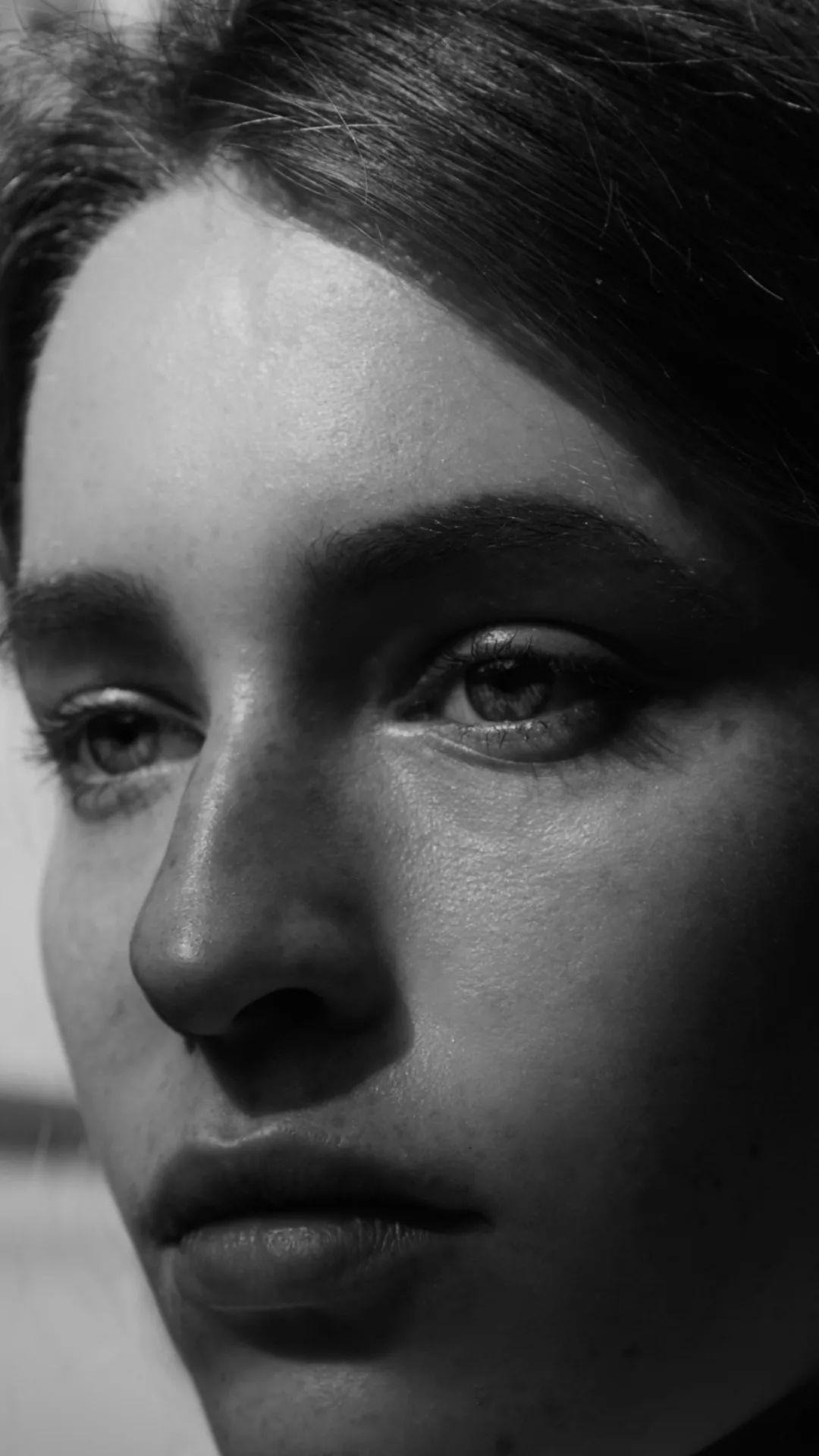 Portret zbliżenie twarzy kobiety w czerni i bieli, z ostrym światłem podkreślającym teksturę skóry i wyraz oczu.