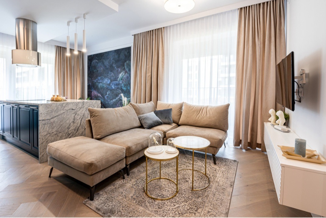 Jasny salon z beżową sofą narożną, marmurowym blatem kuchennym i abstrakcyjną tapetą w odcieniach niebieskiego i zieleni.