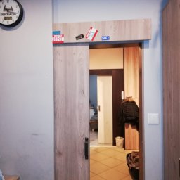 Golden Hands - Drewniane drzwi przesuwne z naklejkami nad ościeżnicą, widok na wnętrze pokoju z płytkami podłogowymi i garderobą