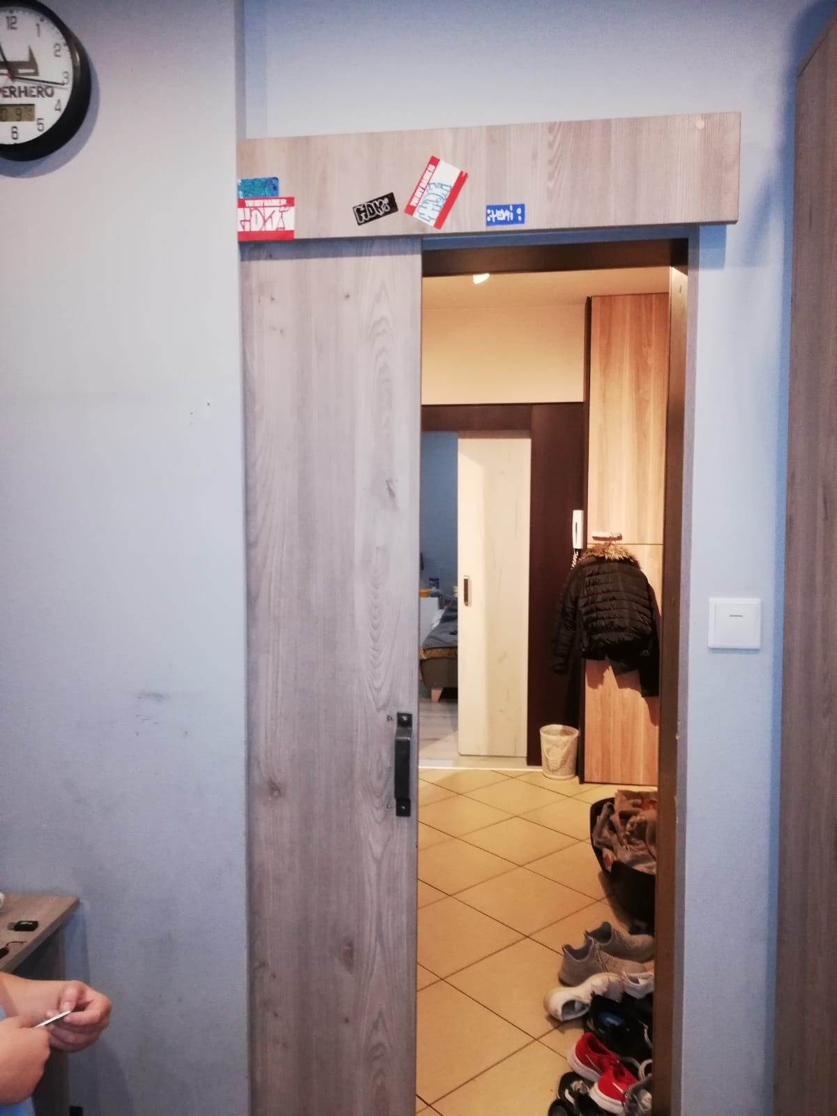 Drzwi przesuwne z drewnopodobnym wykończeniem, otwarte, z naklejkami dekoracyjnymi nad otworem, widok na przedpokój z szafą i kurtką, na podłodze buty.