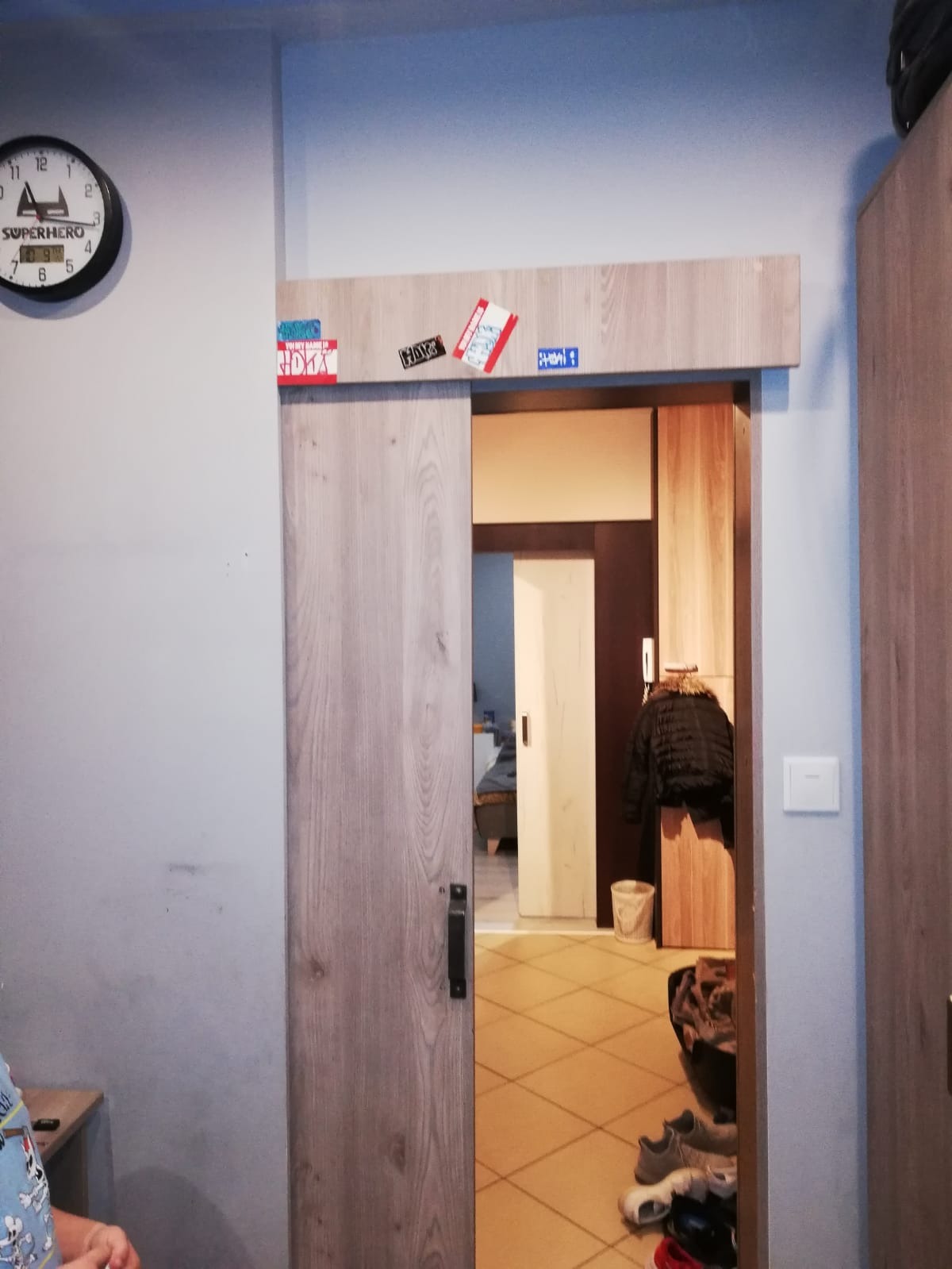 Drewniane drzwi przesuwne z naklejkami nad ościeżnicą, widok na wnętrze pokoju z płytkami podłogowymi i garderobą