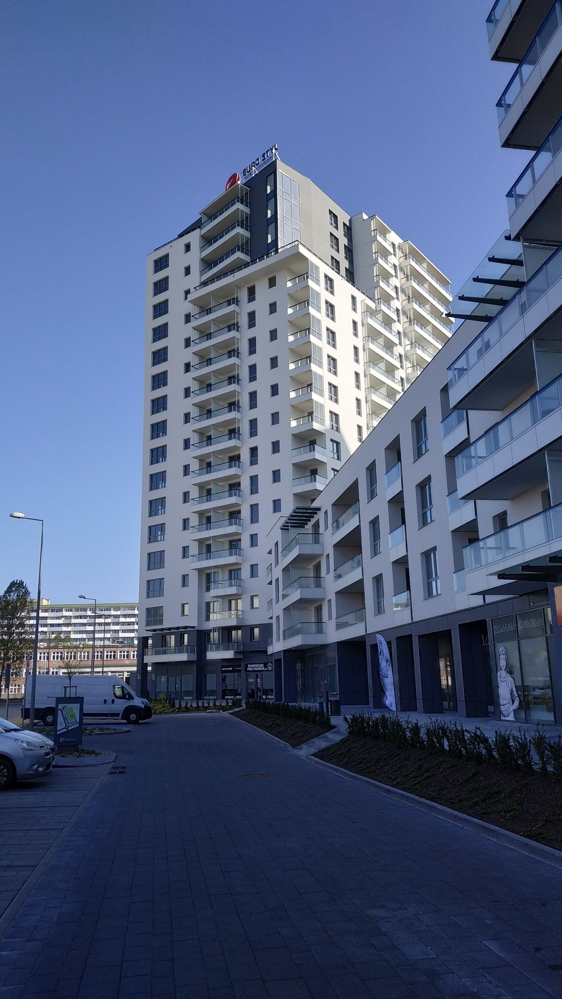 Nowoczesny, wielopiętrowy budynek mieszkalny z balkonami w słoneczny dzień, widok z poziomu chodnika.