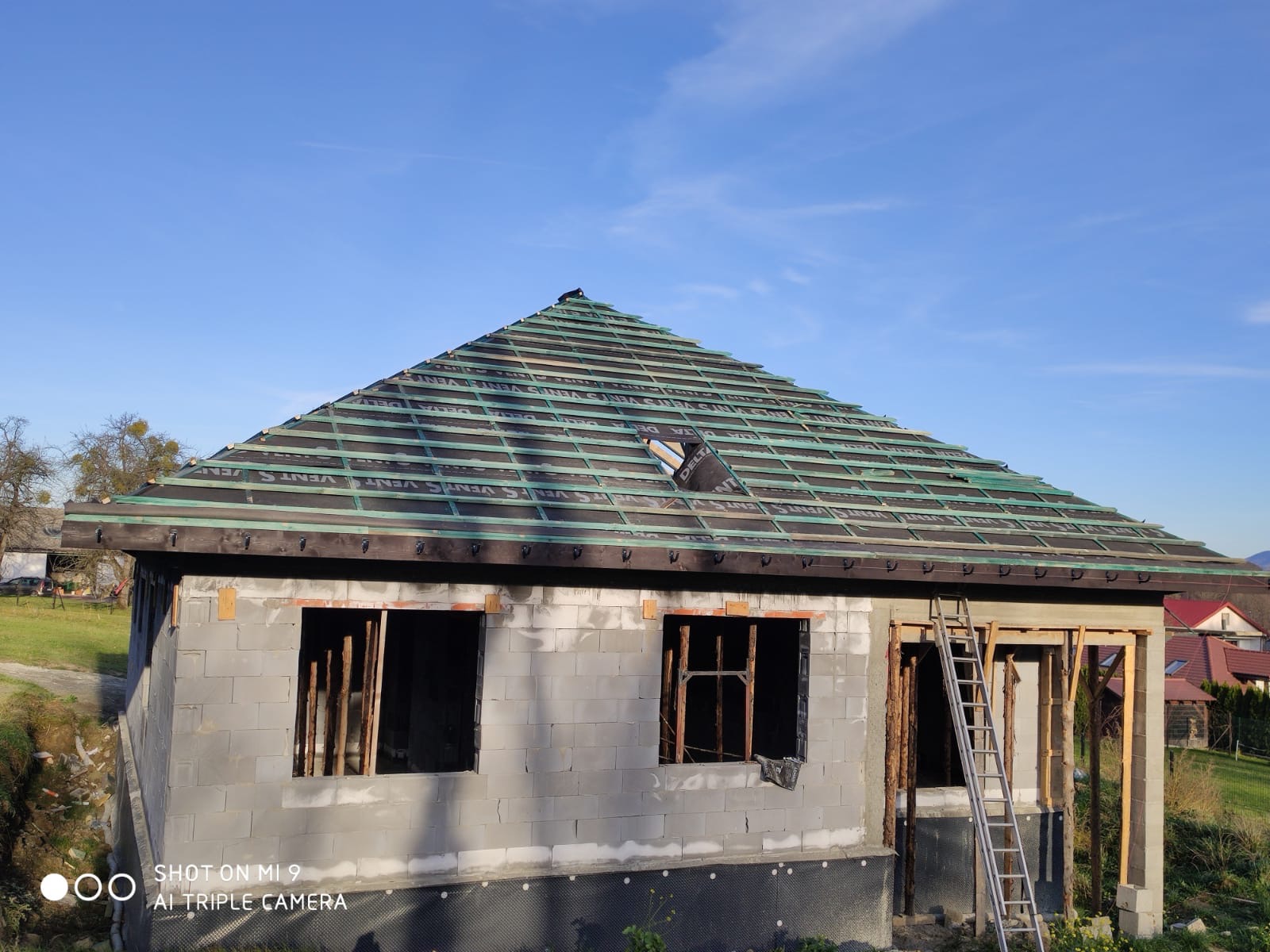 Dom w trakcie budowy, widoczny szkielet dachu z membraną Delta Vent S oraz ściany z bloczków betonowych z otworami okiennymi, drabina oparta o ścianę.