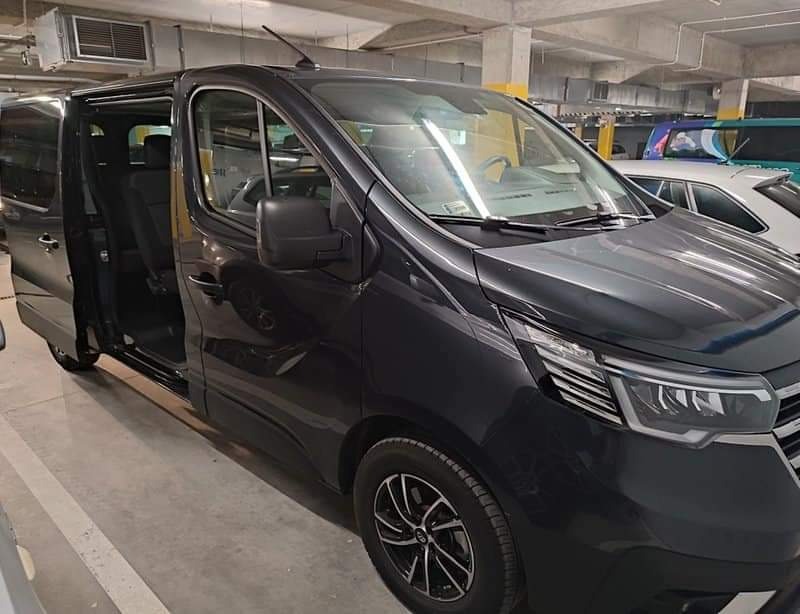 Czarny van z otwartymi drzwiami przesuwnymi, zaparkowany w garażu podziemnym, widoczne fotele wewnątrz.