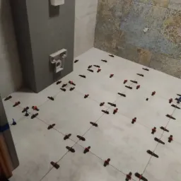 Białe płytki podłogowe w trakcie układania w łazience, widoczne krzyżyki dystansowe i sznurki poziomujące, z elementami instalacji sanitarnych na ścianie.