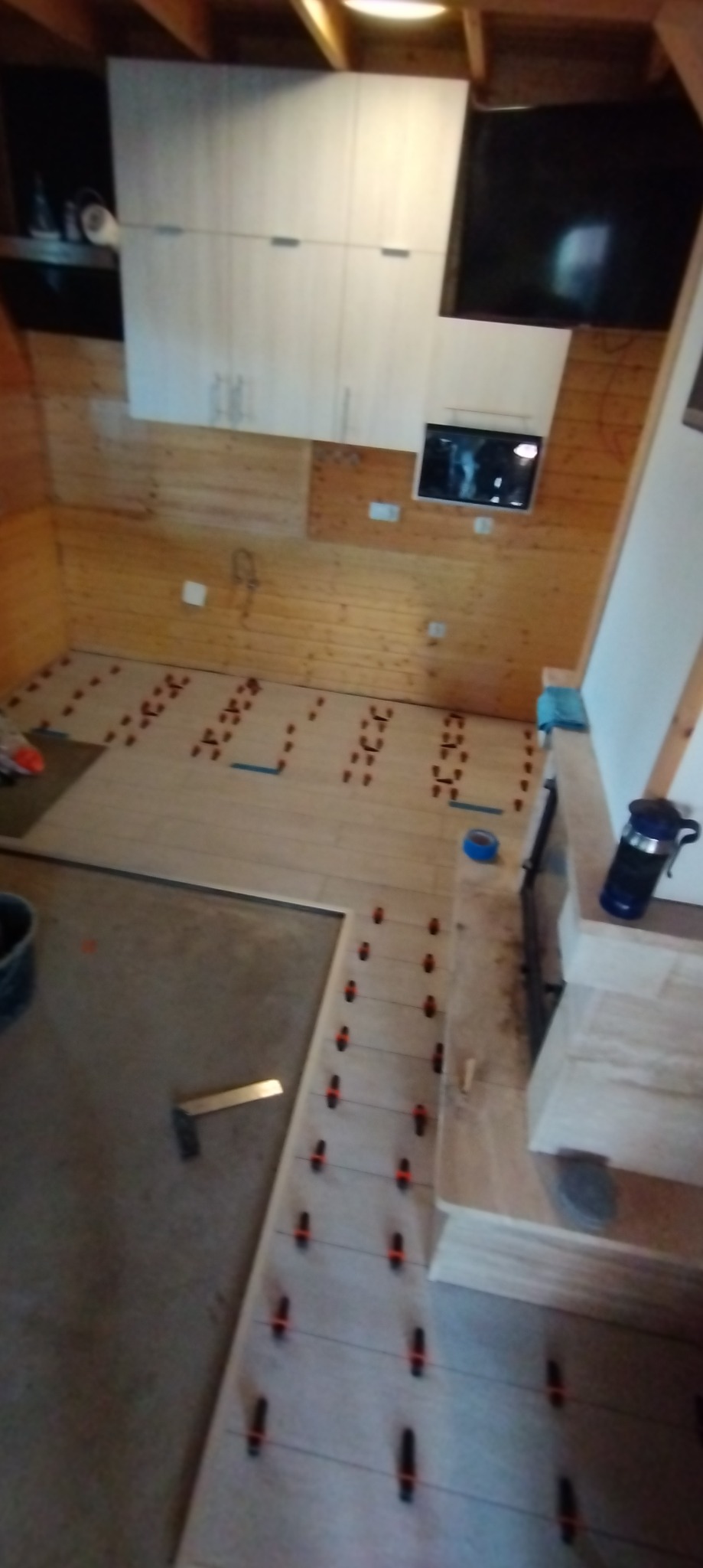 Wnętrze pokoju w Resko z drewnianymi ścianami i podłogą w trakcie układania jasnych paneli, widoczne narzędzia i krzyżyki dystansowe.