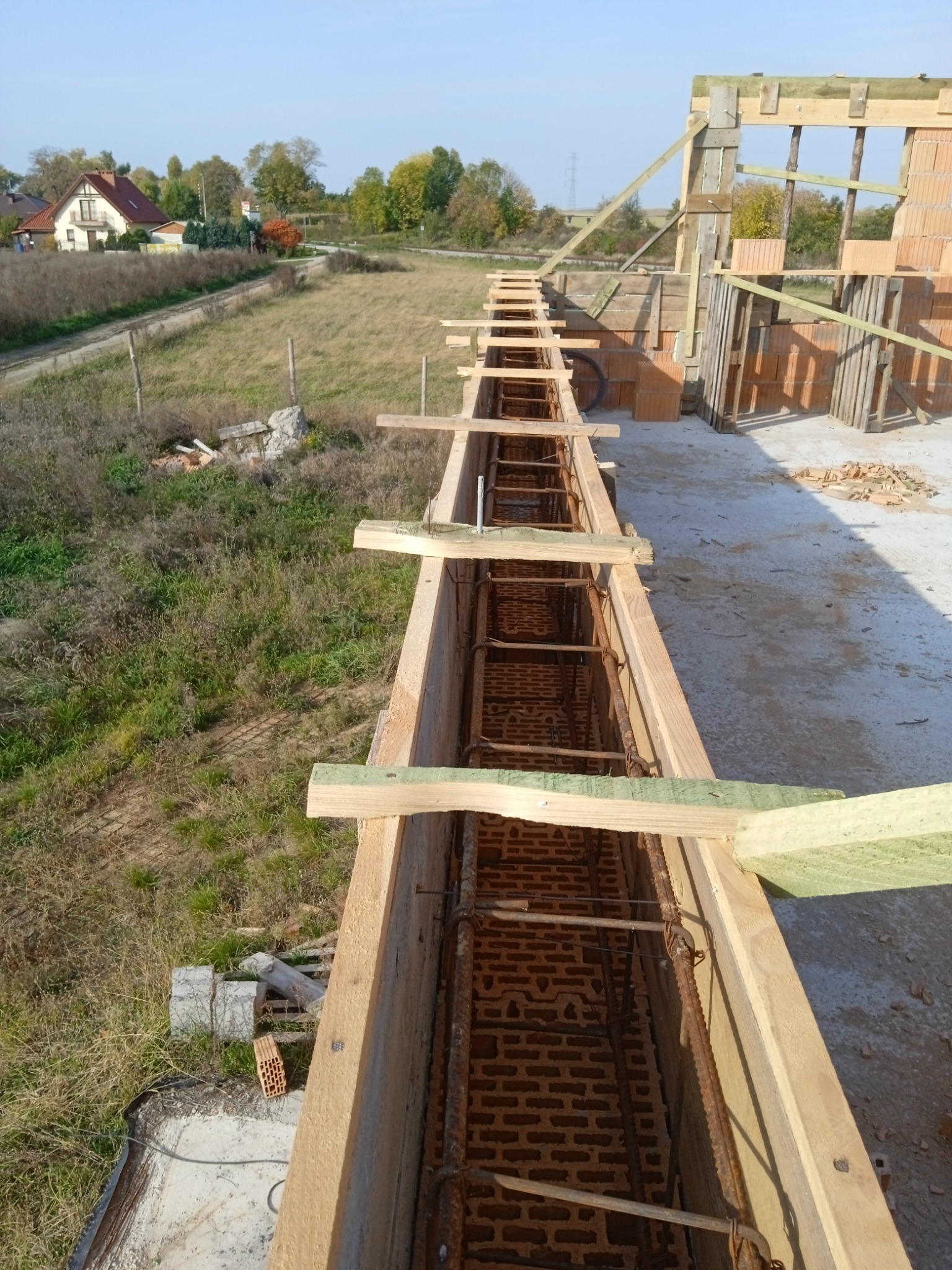 Wieniec żelbetowy w szalunku zbrojony stalą, widok z góry na budowę domu jednorodzinnego w słoneczny dzień.