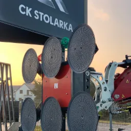 Urządzenie z przyssawkami do montażu szyb, z logo firmy CK Stolarka na tle zachodzącego słońca.