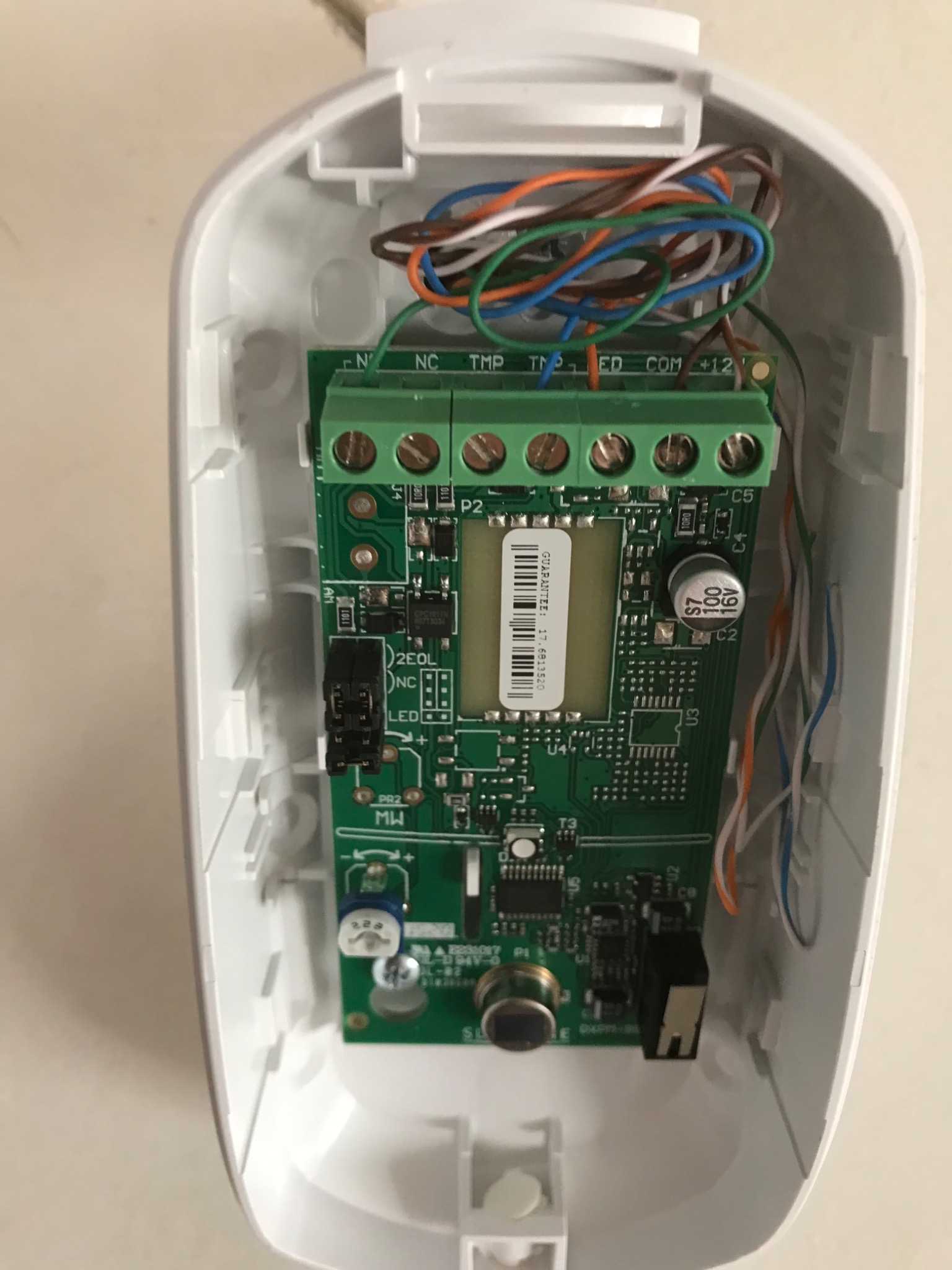 Otwarta obudowa czujnika alarmowego z widoczną płytką drukowaną, złączami śrubowymi i podłączonymi przewodami w różnych kolorach.