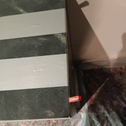 Solid Renovate - Ułożone płytki w czarno-białe pasy, zabezpieczone taśmą i klipsami poziomującymi, widoczne narzędzia glazurnicze i fragment podłogi.