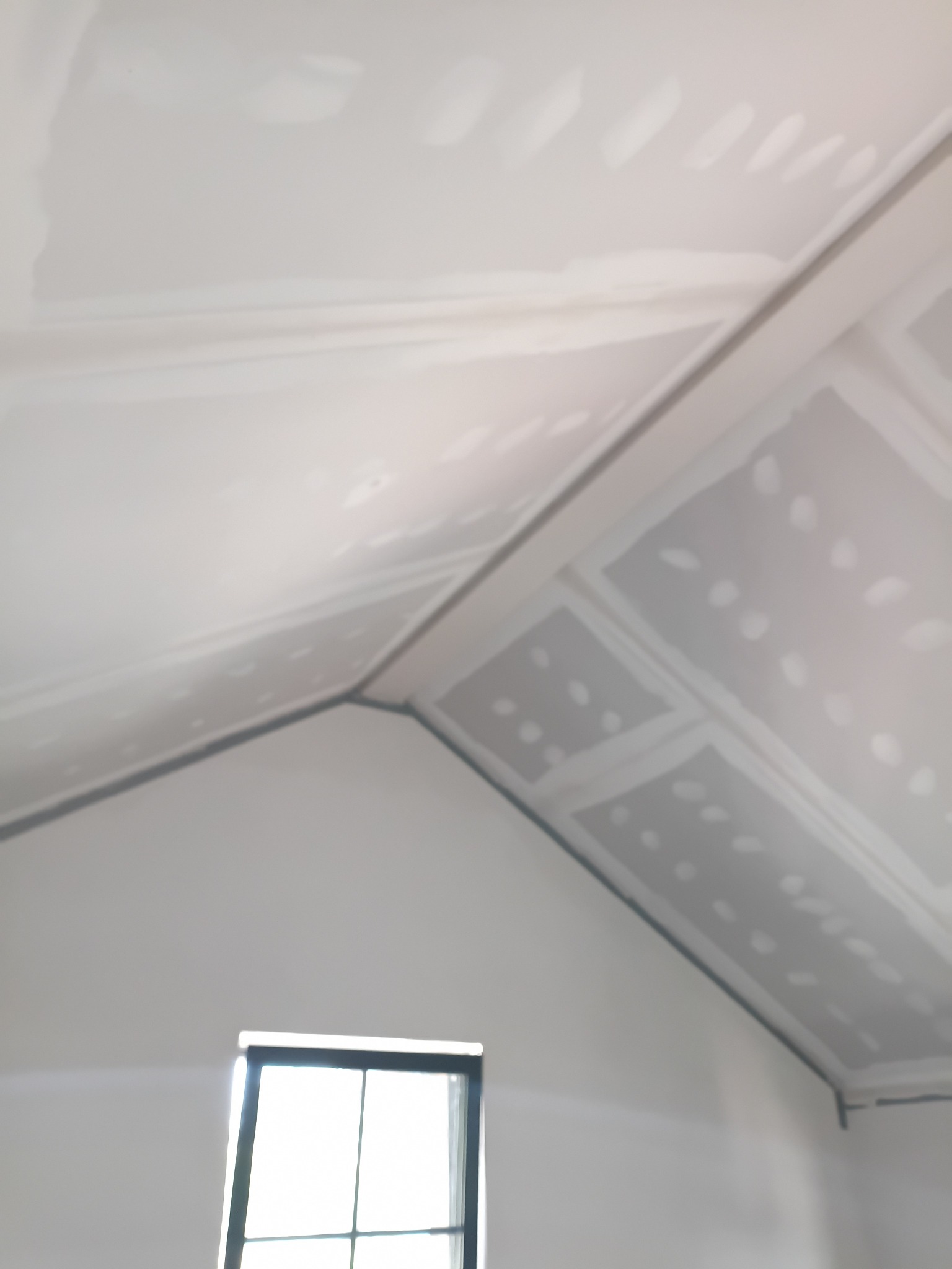 Skośny sufit poddasza z płyt gipsowo-kartonowych, przygotowany do szpachlowania, z widocznym oknem w tle. Etap prac wykończeniowych.