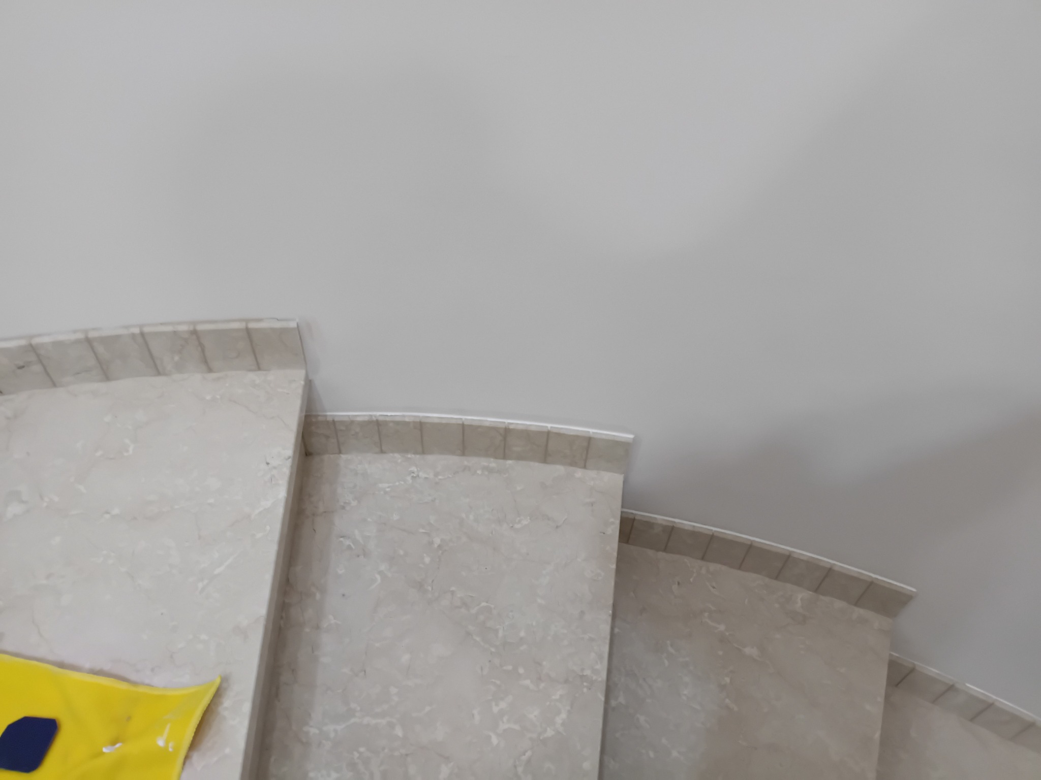 Marmurowe schody w jasnych odcieniach, widok z góry, z żółtą szmatką w rogu. Minimalistyczne ujęcie, skupiające się na fakturze i wzorze kamienia.