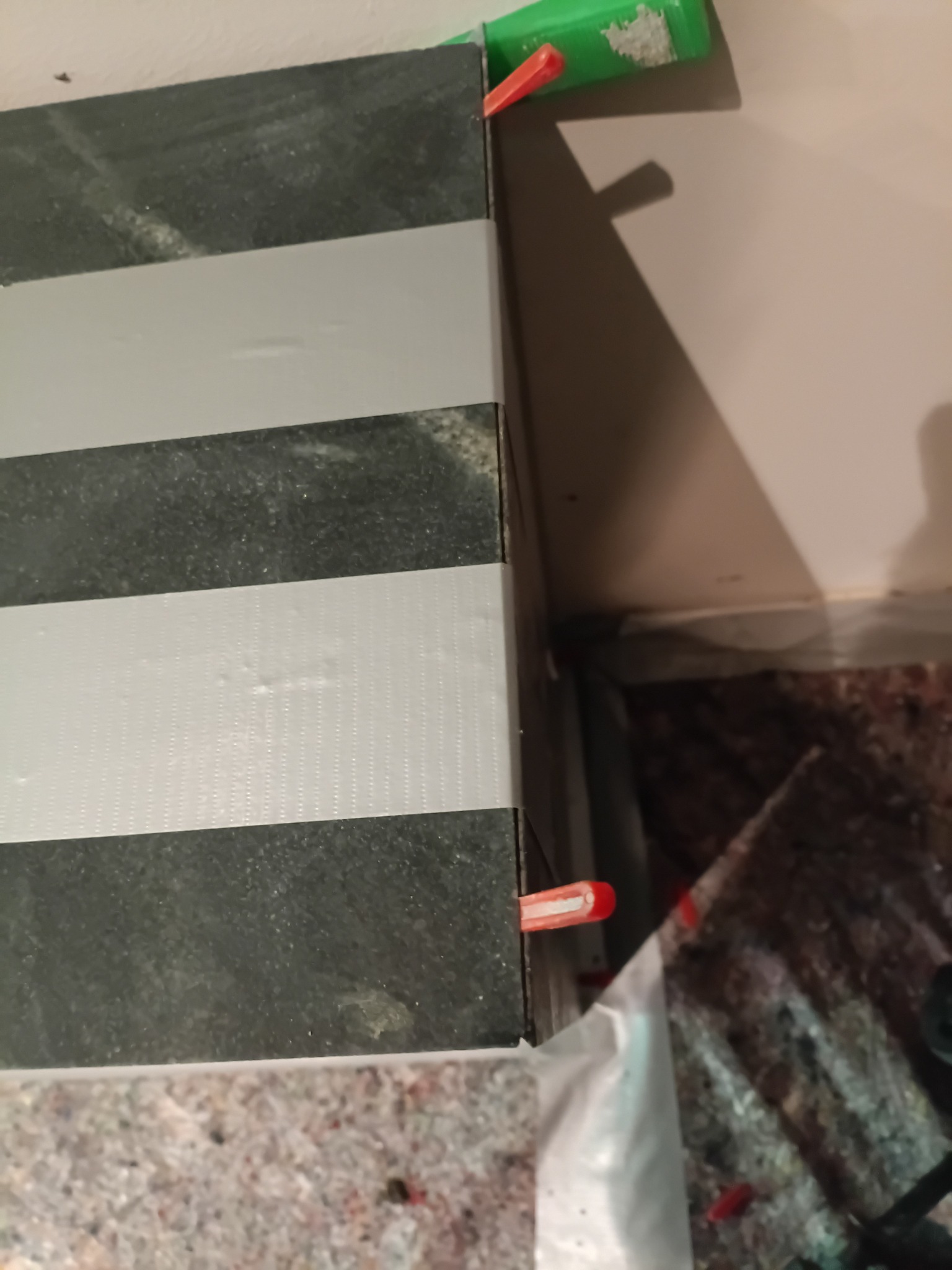 Ułożone płytki w czarno-białe pasy, zabezpieczone taśmą i klipsami poziomującymi, widoczne narzędzia glazurnicze i fragment podłogi.