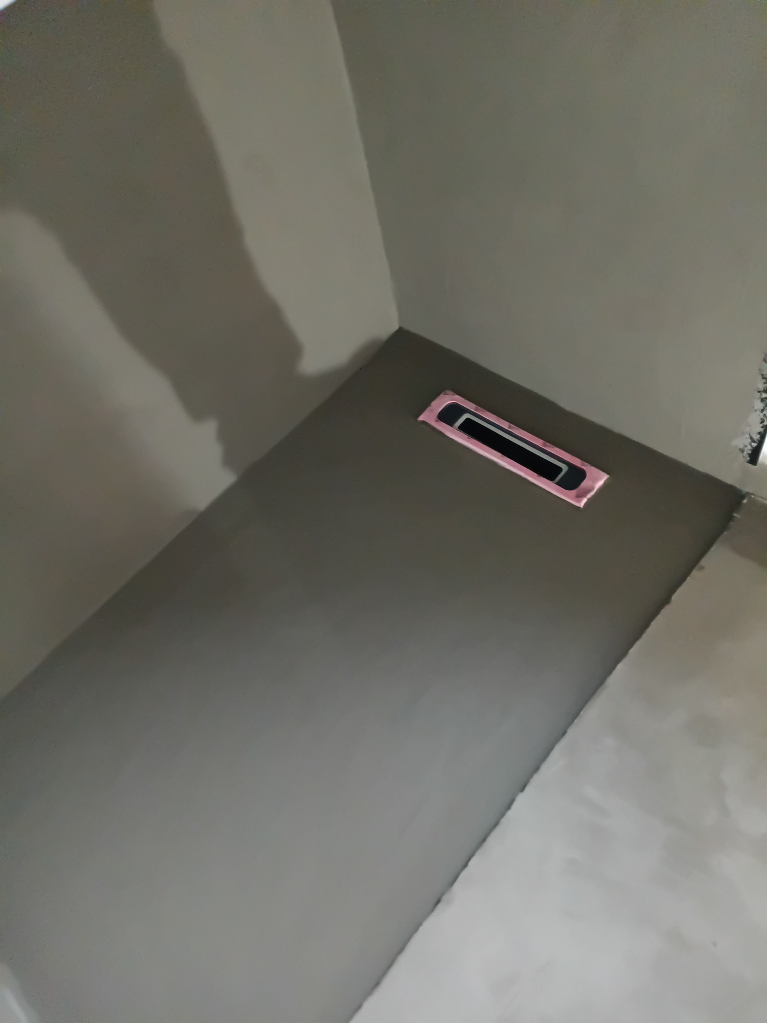 Świeżo nałożona, gładka szpachla na ścianie w rogu pomieszczenia, z widocznym otworem wentylacyjnym zabezpieczonym różową taśmą. Minimalistyczne ujęcie.