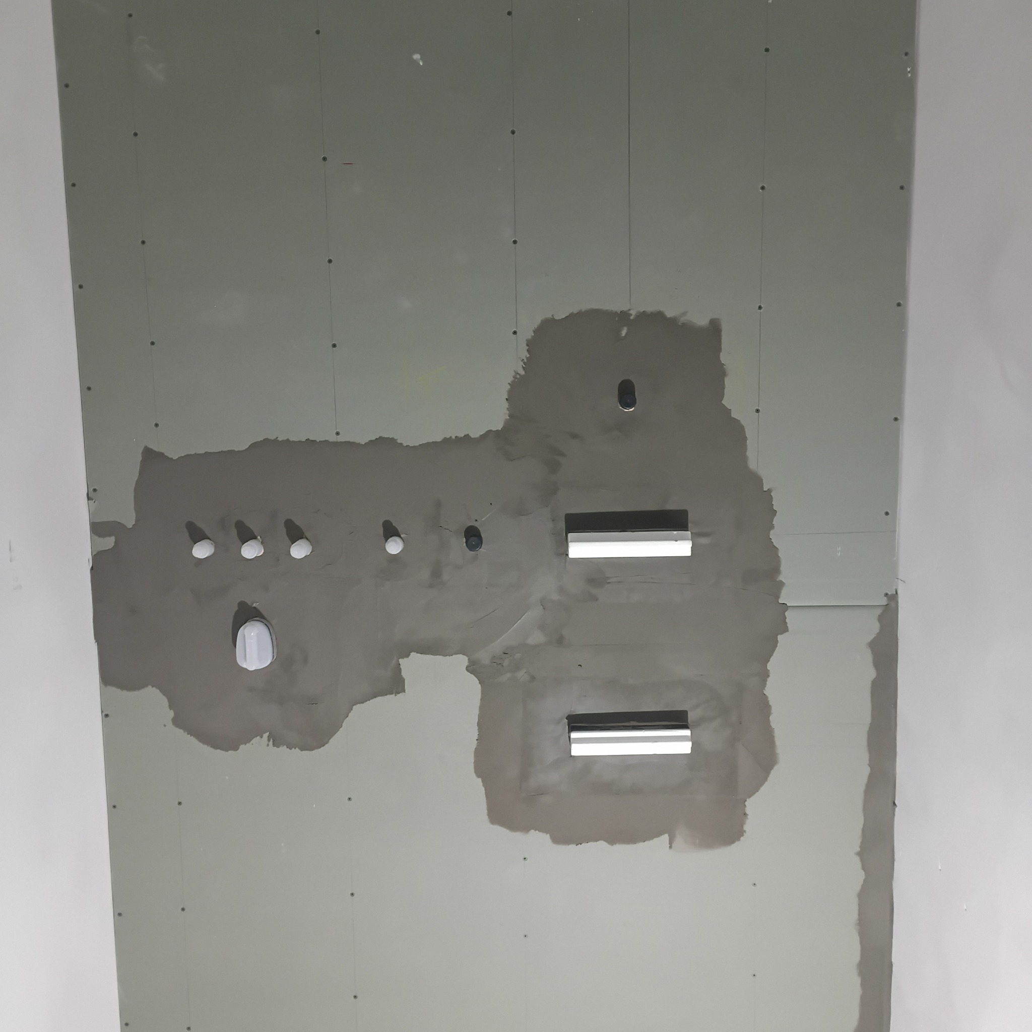 Sufit z płyt gipsowo-kartonowych w trakcie szpachlowania, widoczne otwory na oświetlenie i instalacje. Szpachla w odcieniach szarości, surowy stan wykończenia.