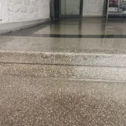 Szlifowane, kamienne schody wejściowe do budynku z widoczną strukturą lastryko i refleksami światła na powierzchni.